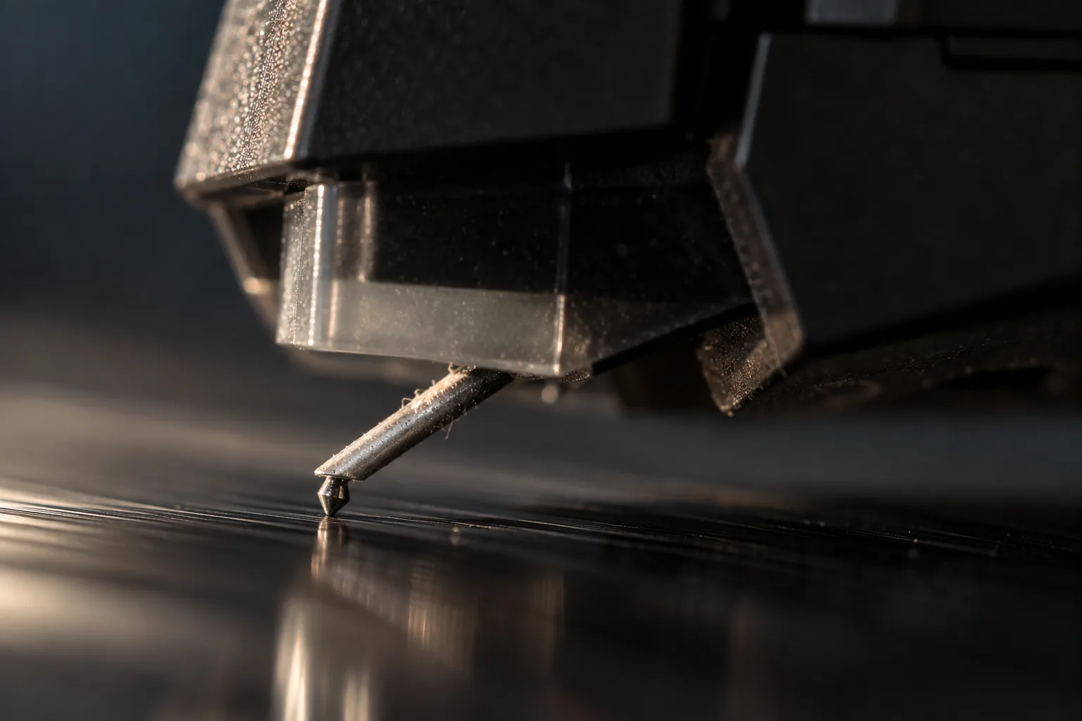 Sterk vergrote opname van een naald: het plastic huis van het element, de dunne metalen cantilever schuin naar beneden en de diamantpunt die de zwarte plaat raakt, met wat grijs stof op de cantilever.